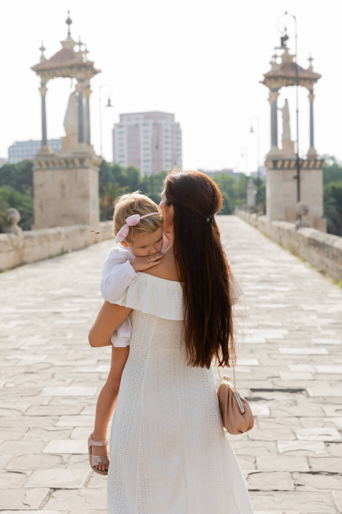 Брюнетка в платье держит ребенка на мосту Пуэнте-дель-Мар в Валенсии - Фото, изображение