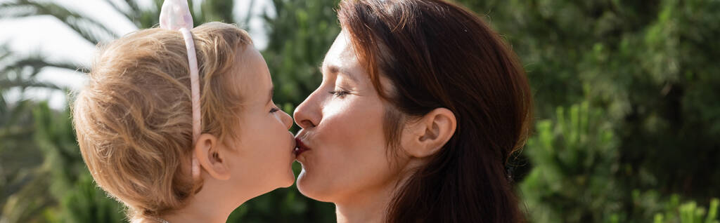 Side view of brunette mother kissing baby daughter outdoors in Valencia, banner  - Fotoğraf, Görsel
