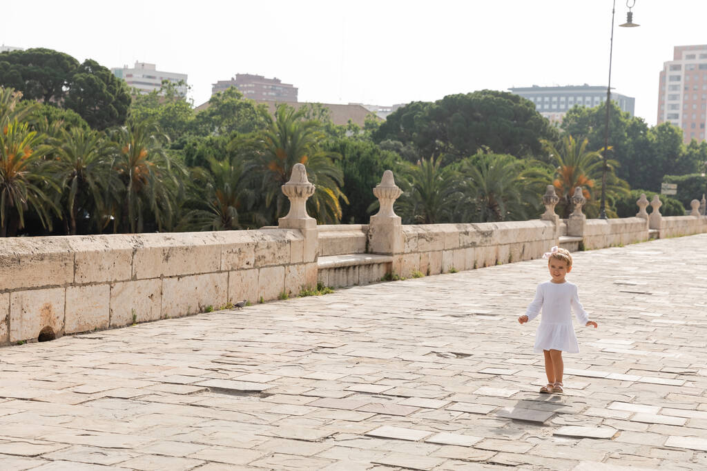 Valencia 'da Puente Del Mar köprüsünde yürüyen beyaz elbiseli, gülümseyen küçük kız. - Fotoğraf, Görsel