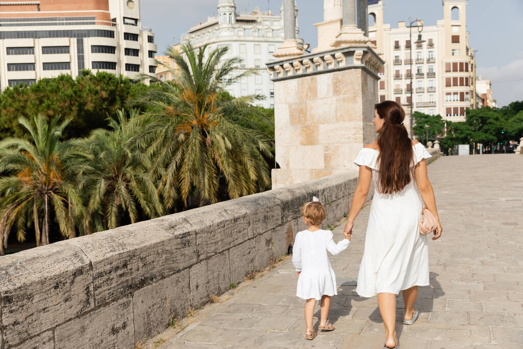Женщина в белом платье держит ребенка за руку во время прогулки по мосту Пуэнте-дель-Мар в Валенсии - Фото, изображение