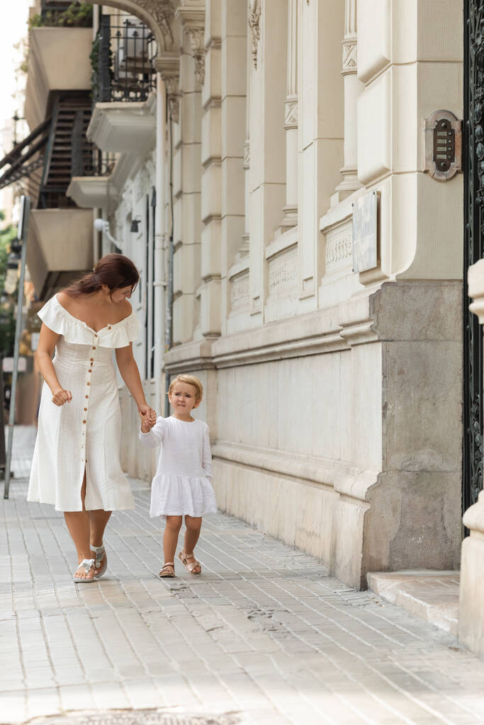 Kobieta i dziecko trzymający się za ręce podczas spaceru ulicą miejską w Walencji - Zdjęcie, obraz