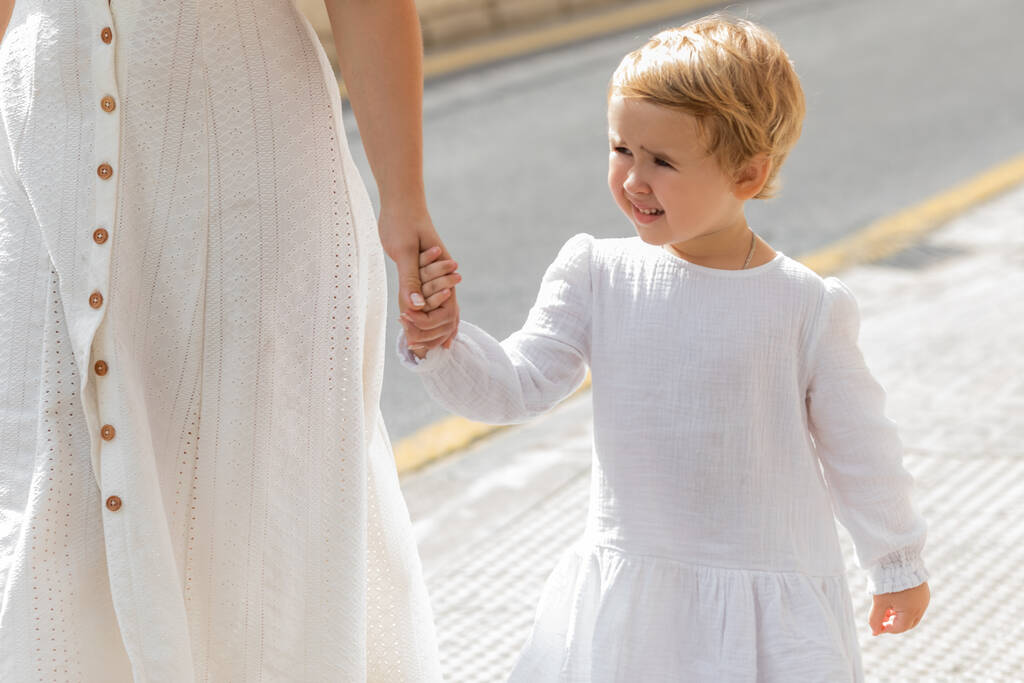 Smiling toddler girl in summer dress holding hand of mother on urban street in Valencia - Foto, Imagen