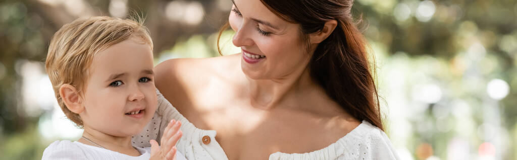 Мати дивиться на усміхненого малюка в літньому парку, банер
  - Фото, зображення