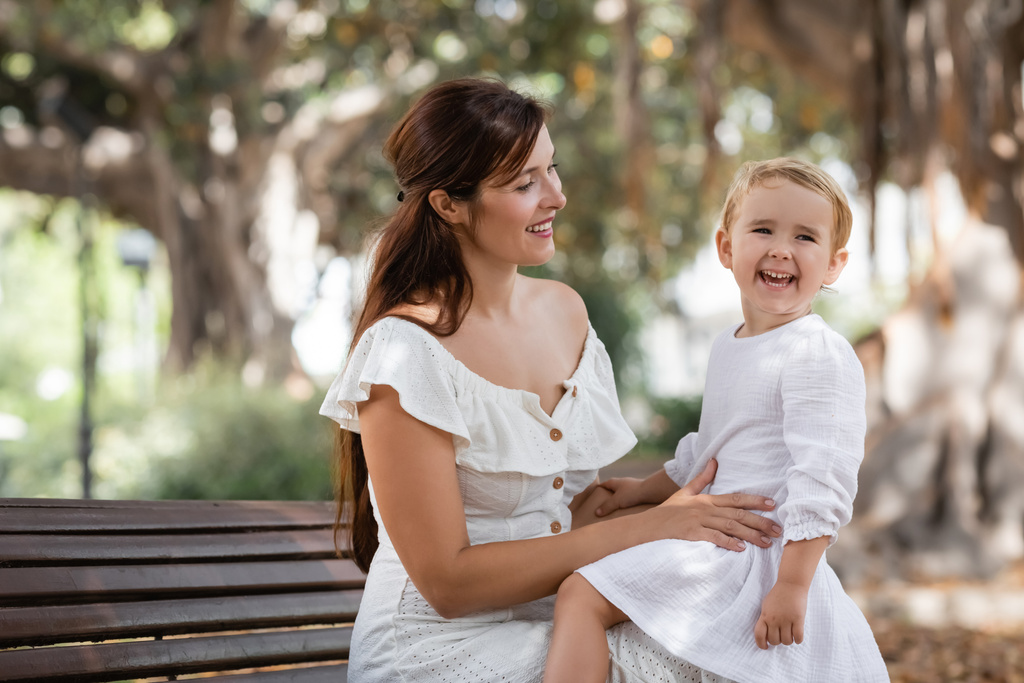Brunette woman looking at daughter laughing on bench in park - Foto, immagini