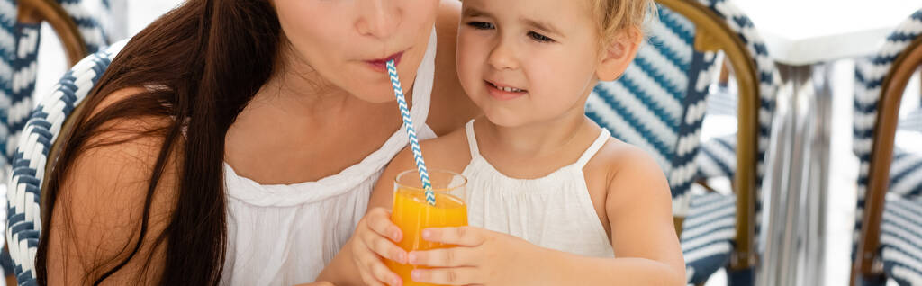 Toddler girl holding orange juice near mom in outdoor cafe, banner  - Photo, image