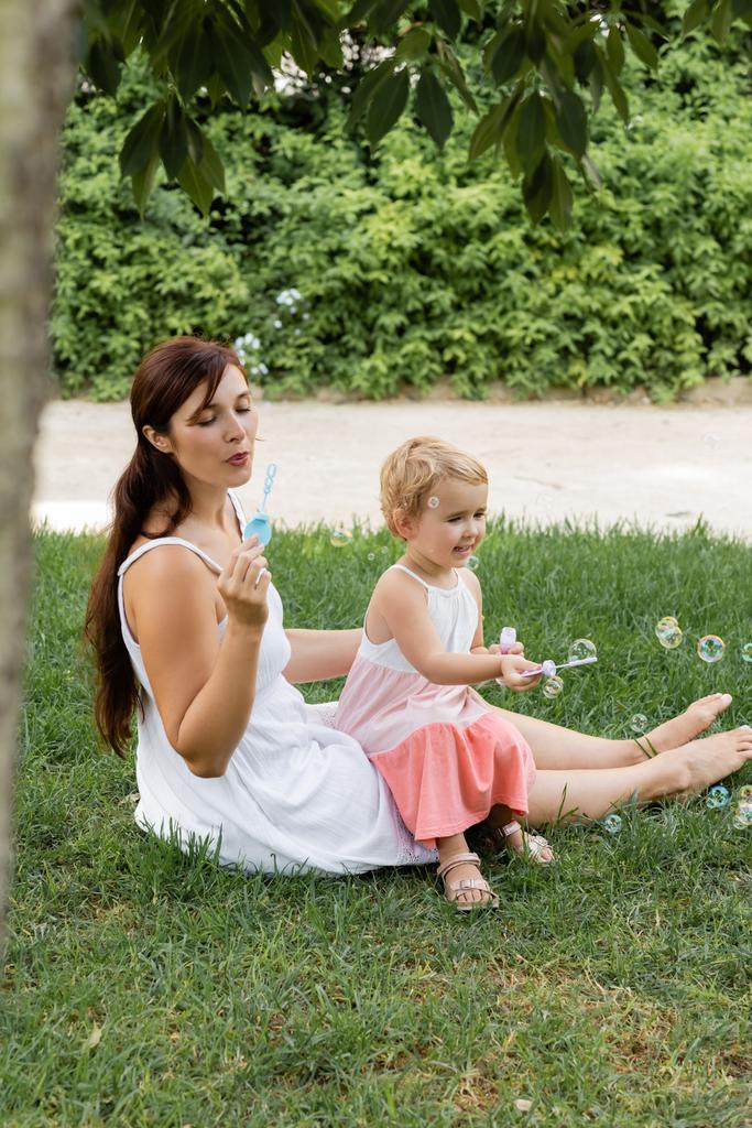 Kobieta i dziecko dmuchanie bańki mydlane na trawniku w parku  - Zdjęcie, obraz