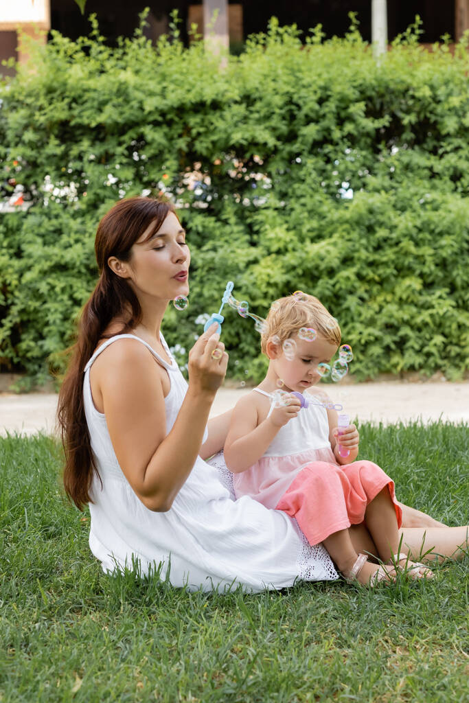 Mother and child blowing soap bubbles on meadow in park  - Foto, afbeelding