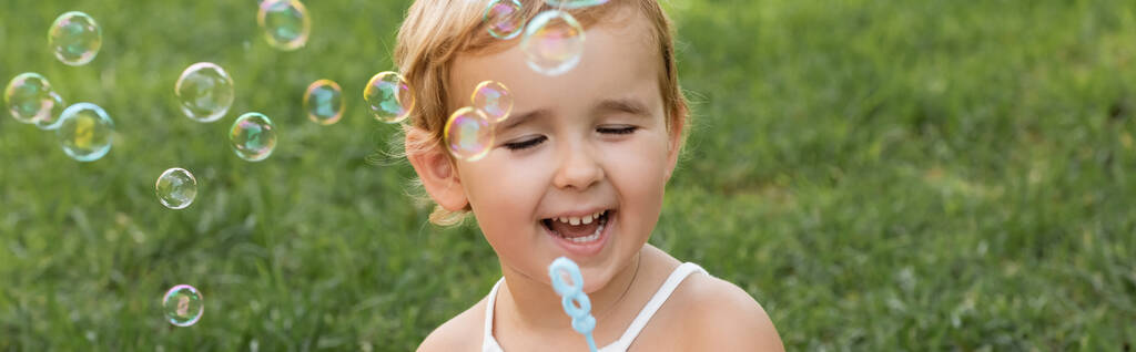 Cheerful baby girl holding wand near soap bubbles in park, banner  - Fotoğraf, Görsel