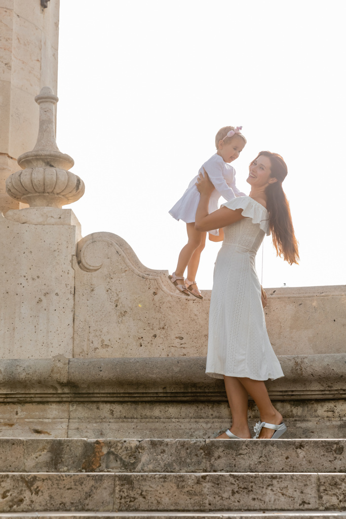 Brunette mother lifting baby daughter in dress on stairs of Puente Del Mar bridge in Spain  - Foto, immagini