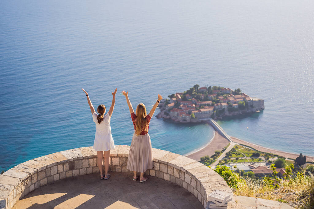 Two Woman tourist on background of beautiful view of the island of St. Stephen, Sveti Stefan on the Budva Riviera, Budva, Montenegro. Travel to Montenegro concept. - Photo, Image