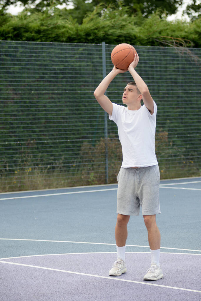 Девятнадцатилетний подросток, стреляющий в кольцо на баскетбольной площадке в общественном парке - Фото, изображение