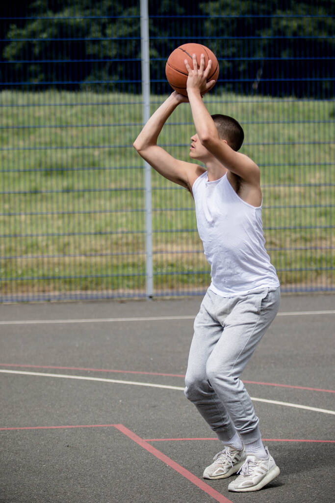 Девятнадцатилетний подросток, стреляющий в кольцо на баскетбольной площадке в общественном парке - Фото, изображение