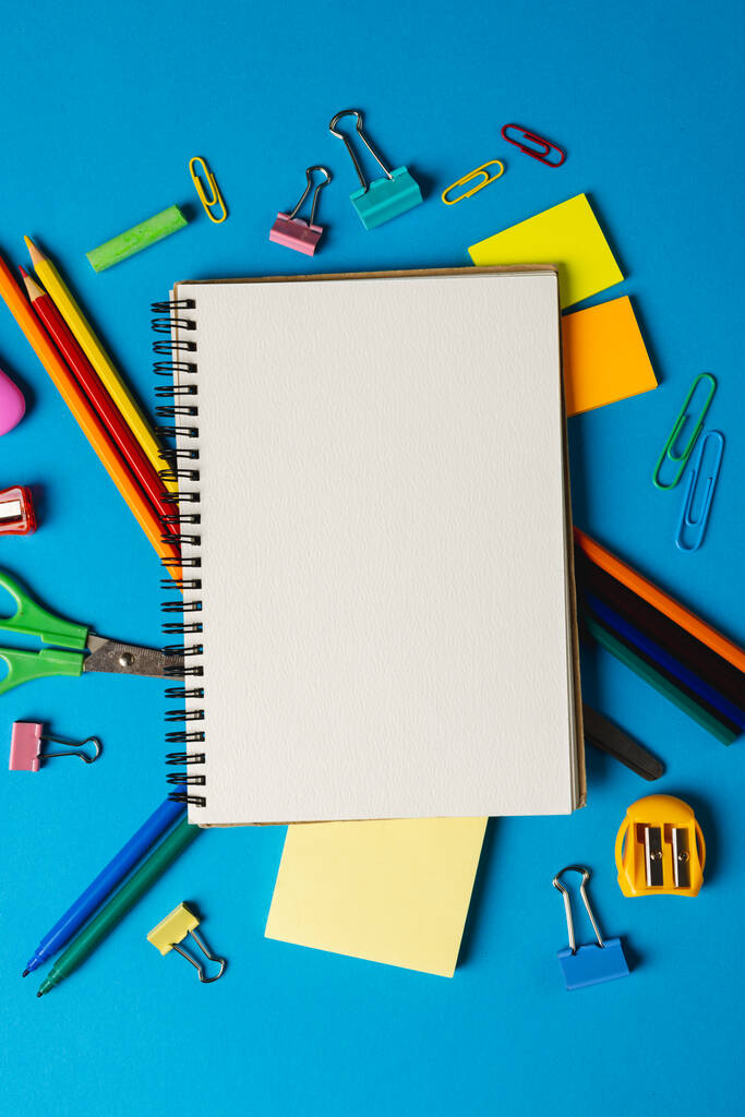 Verticale samenstelling van schoolbenodigdheden met notitieboekje met kopieerruimte op blauw oppervlak. Schooluitrusting, gereedschap en creativiteit. - Foto, afbeelding