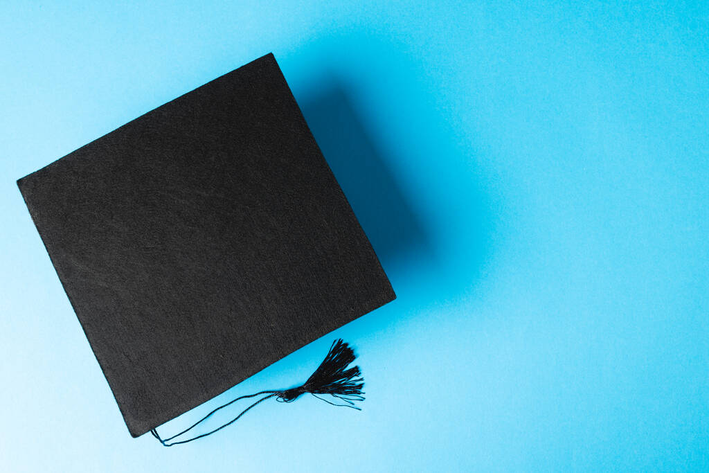 Image of black graduation hat on blue surface with copy space. School, learning, education and graduation concept. - 写真・画像