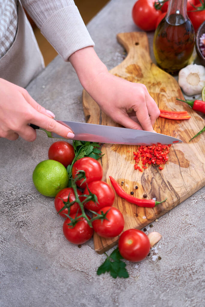 vrouw snijden en chili peper met mes op houten plank. - Foto, afbeelding