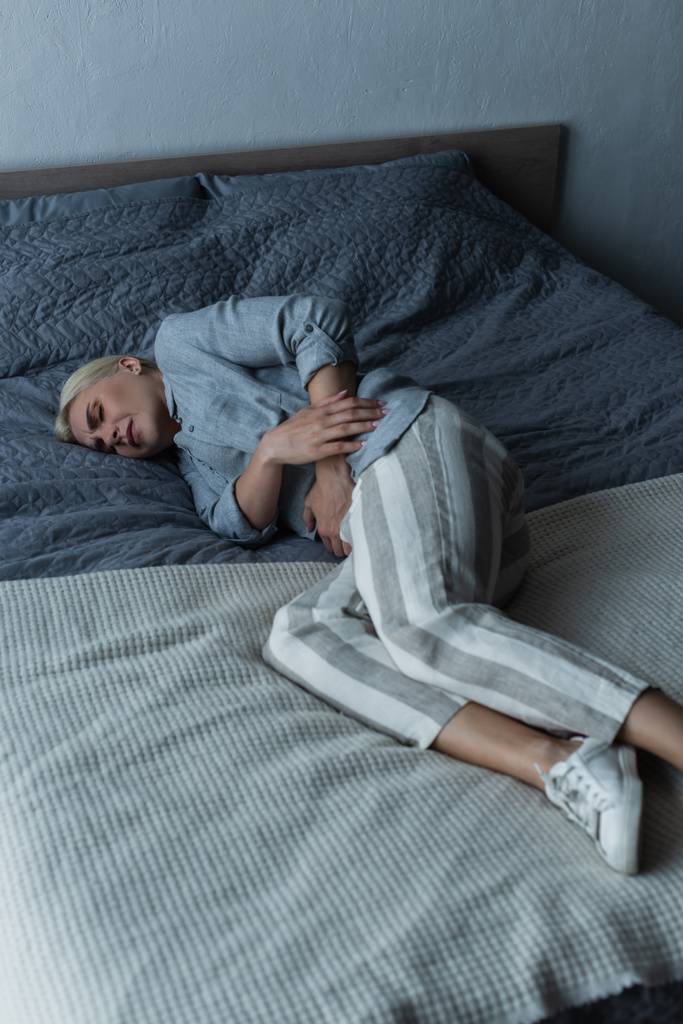 femme blonde avec ménopause souffrant de douleurs abdominales et couchée sur le lit - Photo, image
