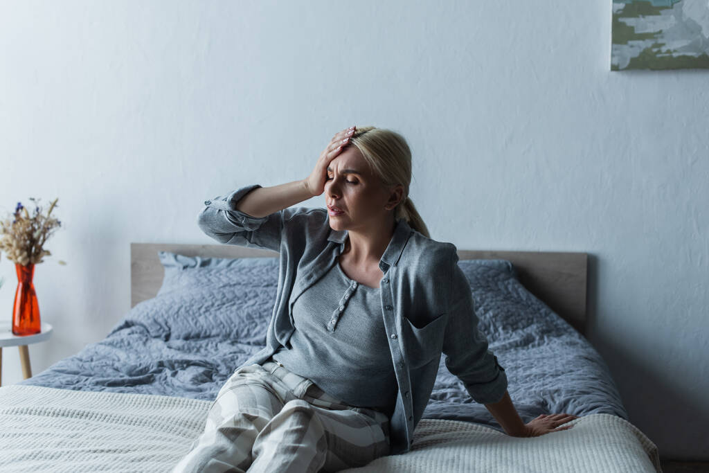 засмучена блондинка з менопаузою страждає від мігрені в спальні
 - Фото, зображення