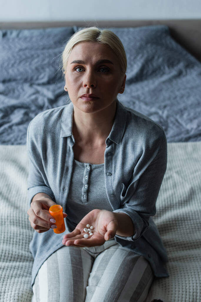 chateado mulher loira com menopausa segurando garrafa e pílulas nas mãos - Foto, Imagem