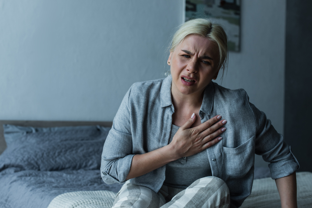 mujer rubia agotada tocando el pecho y sintiendo dolor durante la menopausia  - Foto, Imagen