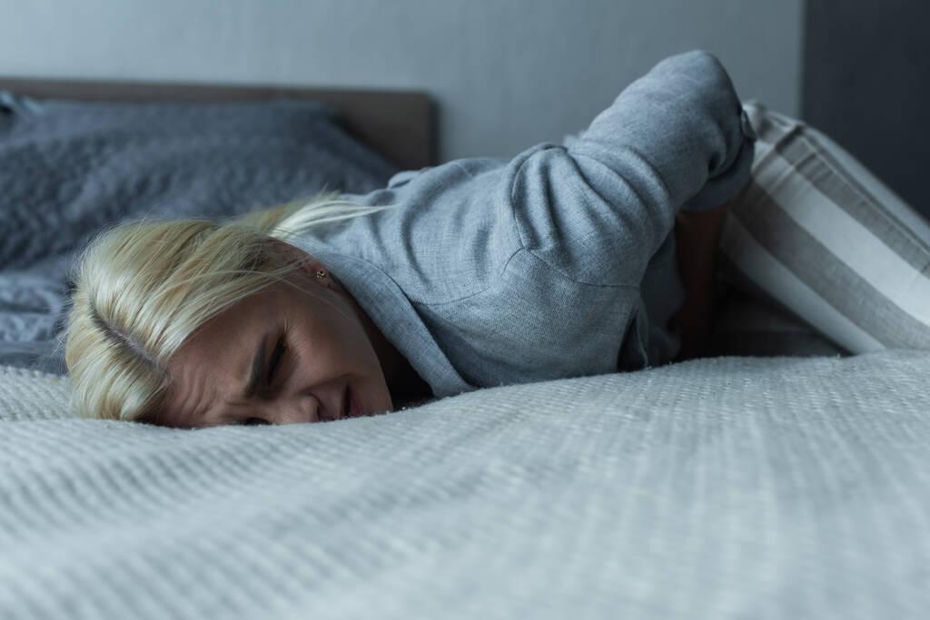mulher estressada deitada na cama enquanto sente dor no estômago durante a menopausa  - Foto, Imagem