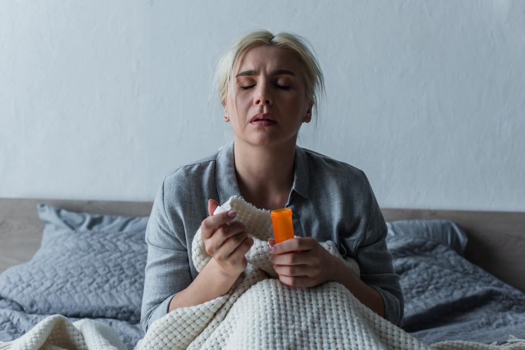 Traurige Frau mit Höhepunkt sitzt im Bett und hält Flasche mit Schmerzmitteln in der Hand  - Foto, Bild