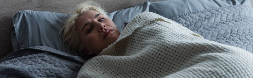 donna bionda depressa con menopausa sdraiata sotto una coperta a letto, striscione - Foto, immagini