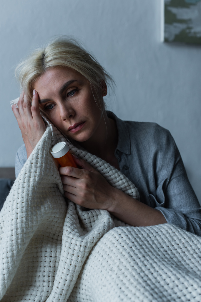 depressed blonde woman with menopause holding bottle with sleeping pills in bed - Fotografie, Obrázek