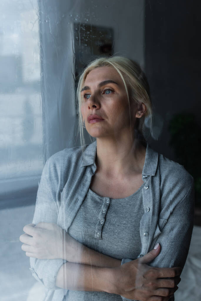 depressieve blonde vrouw kijken naar venster met regen druppels  - Foto, afbeelding