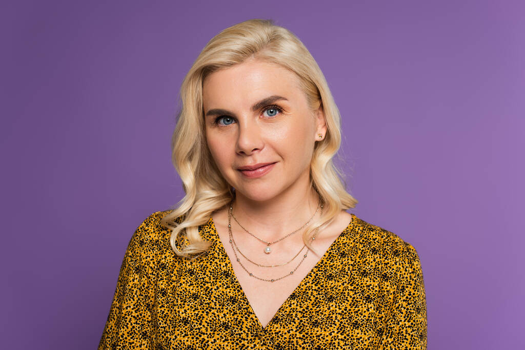 happy and blonde woman in blouse looking at camera isolated on purple  - Photo, image