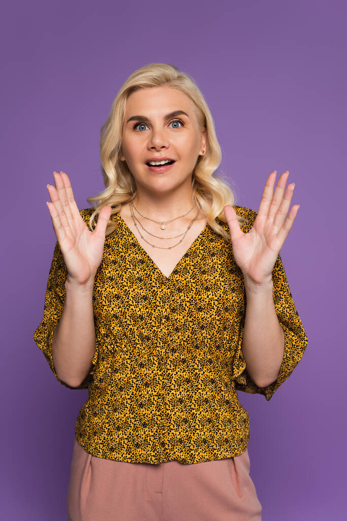 amazed and blonde woman in blouse gesturing isolated on purple  - Foto, afbeelding