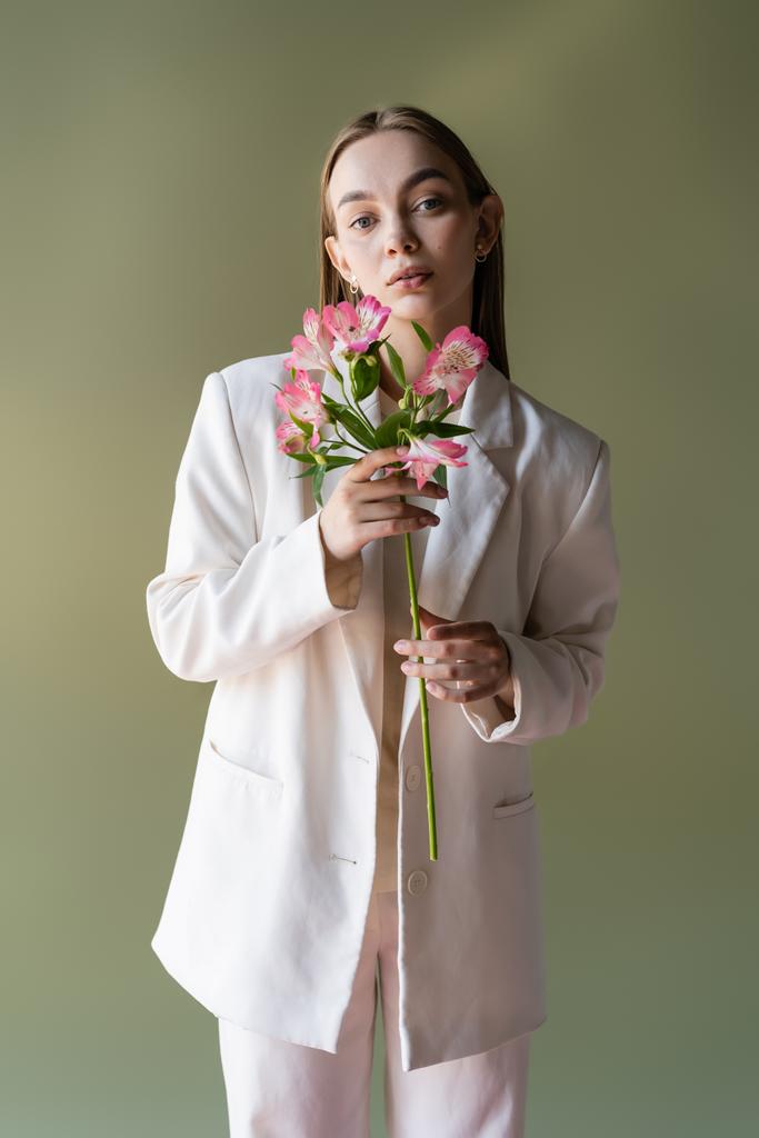 młoda kobieta w białej marynarce gospodarstwa różowe kwiaty alstroemeria izolowane na zielono - Zdjęcie, obraz