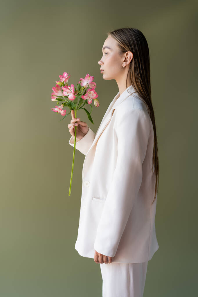 side view of woman in white blazer posing with branch of alstroemeria isolated on green - Valokuva, kuva