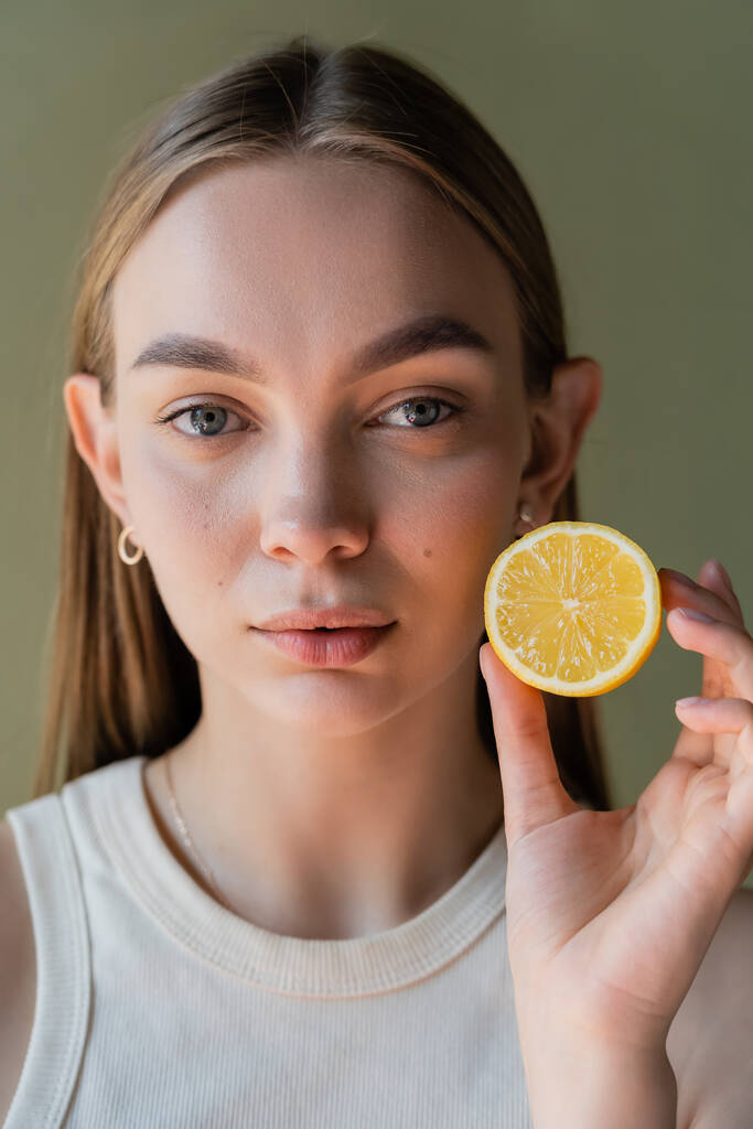 portrait of pretty young woman showing half of juicy lemon isolated on green - Foto, afbeelding