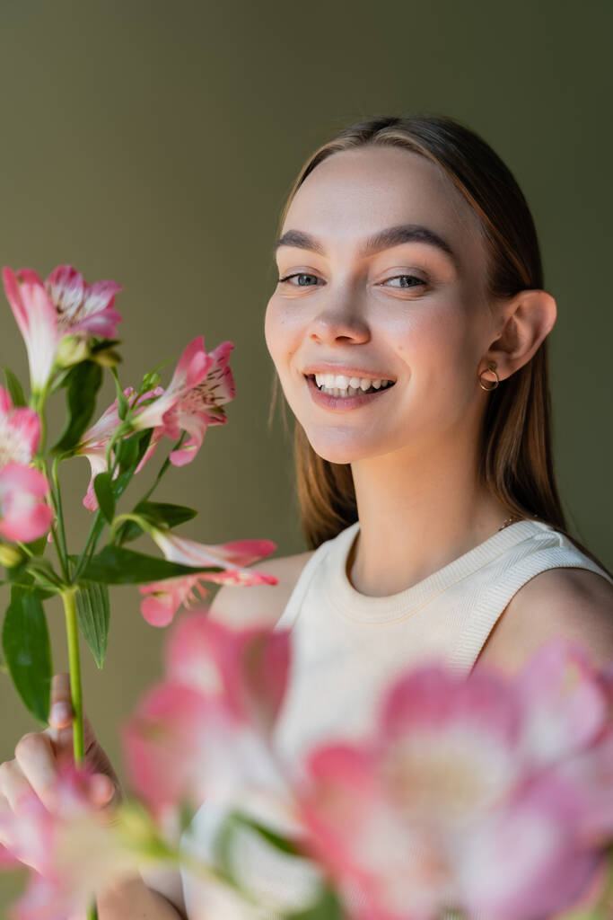 young and happy woman with pink alstroemeria flowers isolated on green - Foto, Imagen