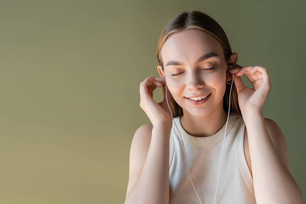 joyful woman with closed eyes listening music in wired earphones isolated on green - Fotoğraf, Görsel