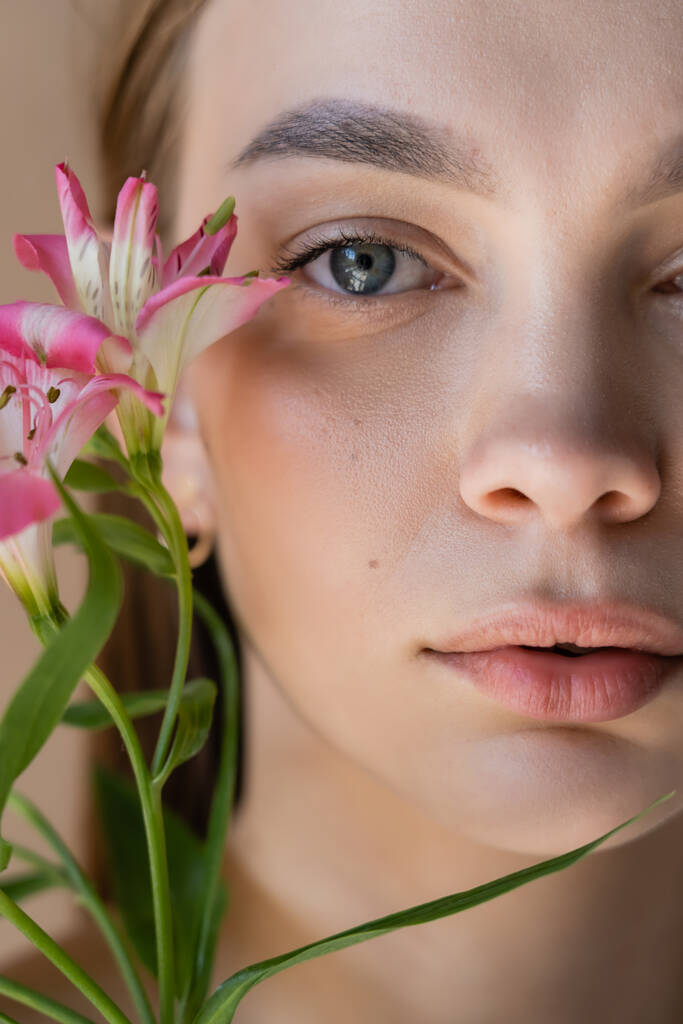 zbliżenie portret przyciętej kobiety z idealną skórą w pobliżu różowe kwiaty alstroemeria - Zdjęcie, obraz
