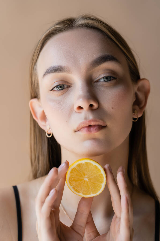 portrait of pretty young woman with perfect skin holding half lemon isolated on beige - Foto, Bild