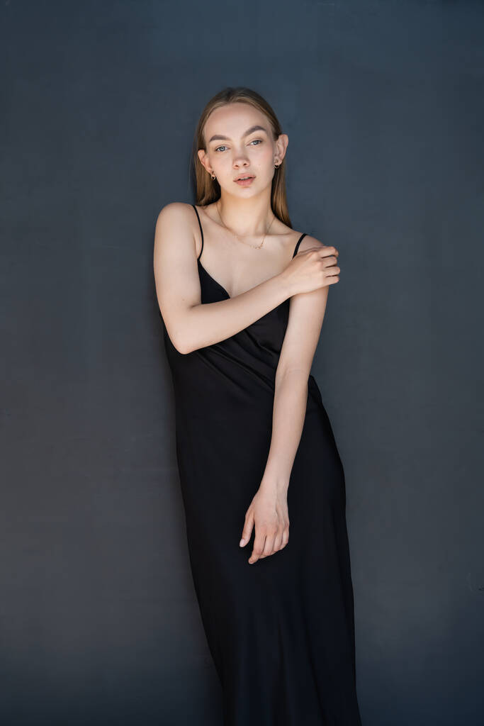 young woman in black strap dress looking at camera on dark background - 写真・画像