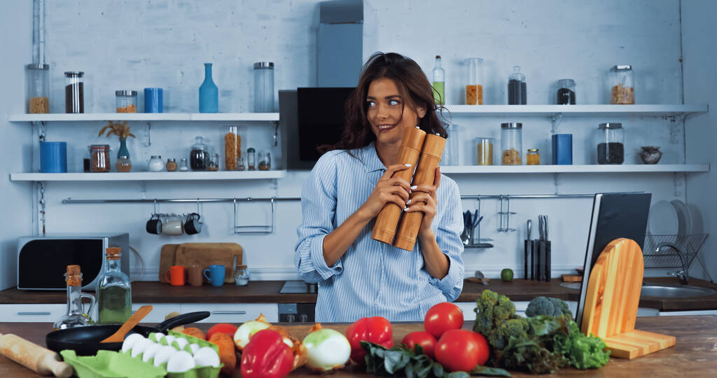 femme brune joyeuse avec des moulins à épices près des légumes crus et des œufs dans la cuisine - Photo, image