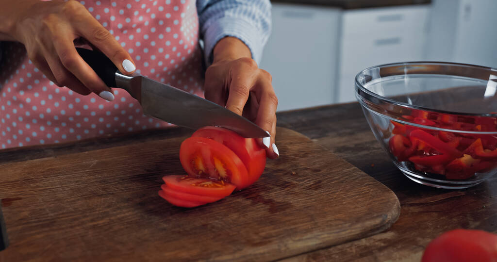 cropped view of woman cutting red tomato near bowl with chopped bell pepper - Foto, Bild
