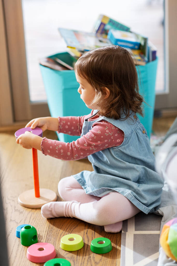 Kinder-, Freizeit- und Personenkonzept - kleines Mädchen spielt zu Hause mit Spielzeugpyramide - Foto, Bild