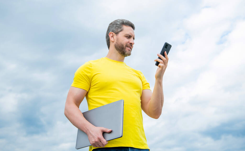 uomo con computer portatile utilizzando il telefono su sfondo cielo. - Foto, immagini