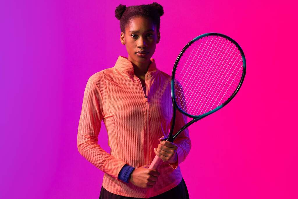 Imagem de uma jogadora de ténis afro-americana com raquete em iluminação rosa neon. Esporte, movimento, fitness e conceito de estilo de vida ativo. - Foto, Imagem