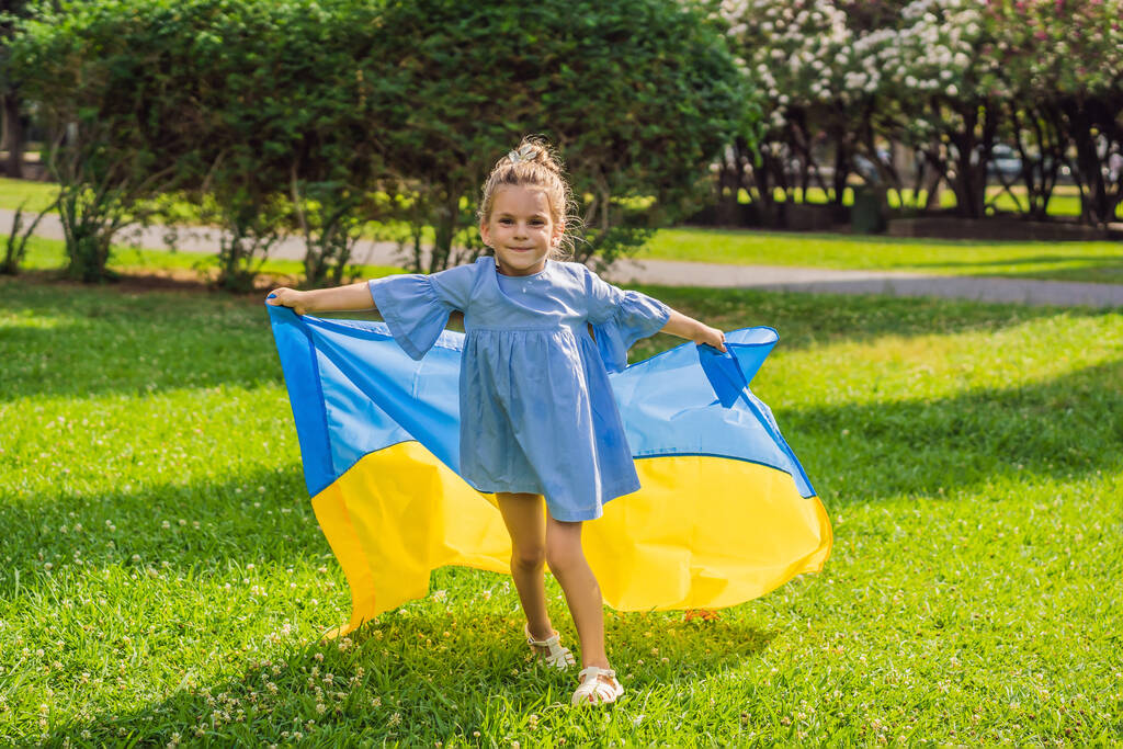 Ukrainian girl with flag of Ukraine. Outside. Concept of problem of war in Europe, supporting of families and children, migrants, emigration, patriotism, motherhood. - Foto, imagen