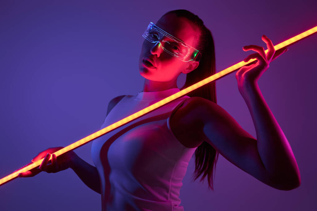 Femme attrayante dans des lunettes futuristes tenant la lampe LED sur fond sombre - Photo, image