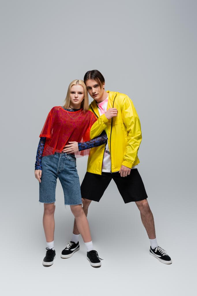 jong paar in trendy kleding poseren op grijze achtergrond - Foto, afbeelding