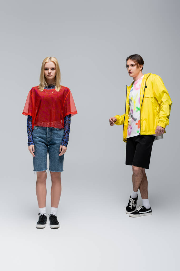 Stylish young man in yellow windbreaker looking at girlfriend on grey background - Foto, Imagen