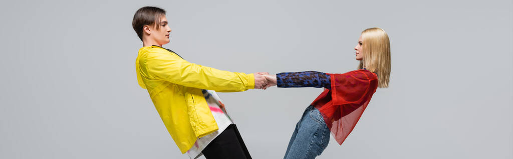 Side view of young couple in bright clothes holding hands isolated on grey, banner  - 写真・画像