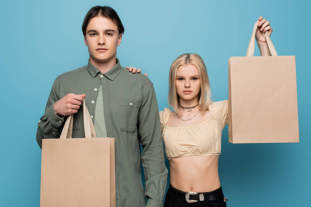 Pretty woman holding shopping bag and touching boyfriend isolated on blue  - Foto, afbeelding
