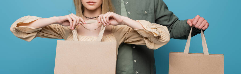 Cropped view of woman holding shopping bag near boyfriend isolated on blue, banner  - Photo, image